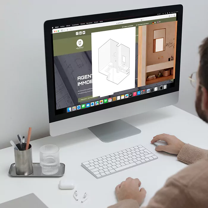 Mann arbeitet am Schreibtisch vor Monitor mit geöffneter Hyfinit-Website und 3D-Immobilienmodell im Browserfenster.